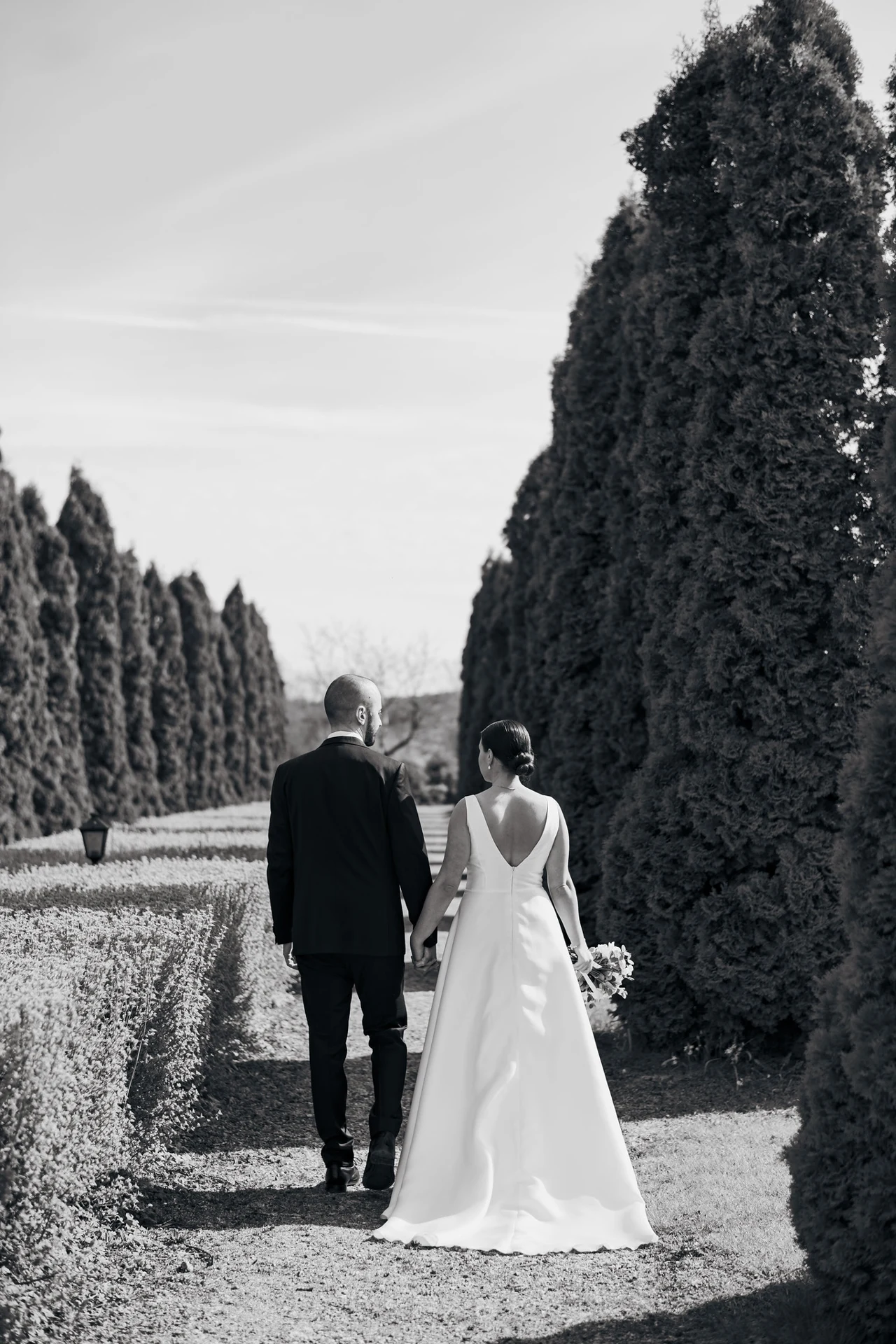 A wedding couple walking along a tree-lined path in black and white.